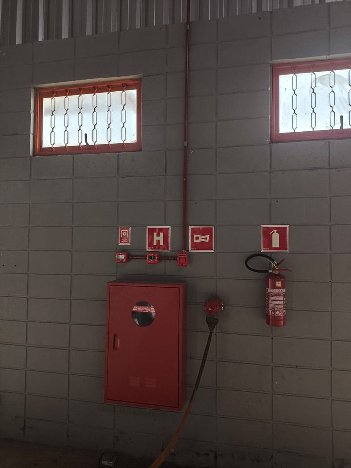 Parede de galpão com abrigo de hidrante, extintor, acionadores de alarme e placas de sinalização de equipamentos
